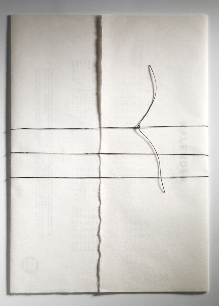 Une feuille de papier à bords déchirés, fendue verticalement, traversée de trois fils tendus à l'horizontale et d'un quatrième qui serpente.