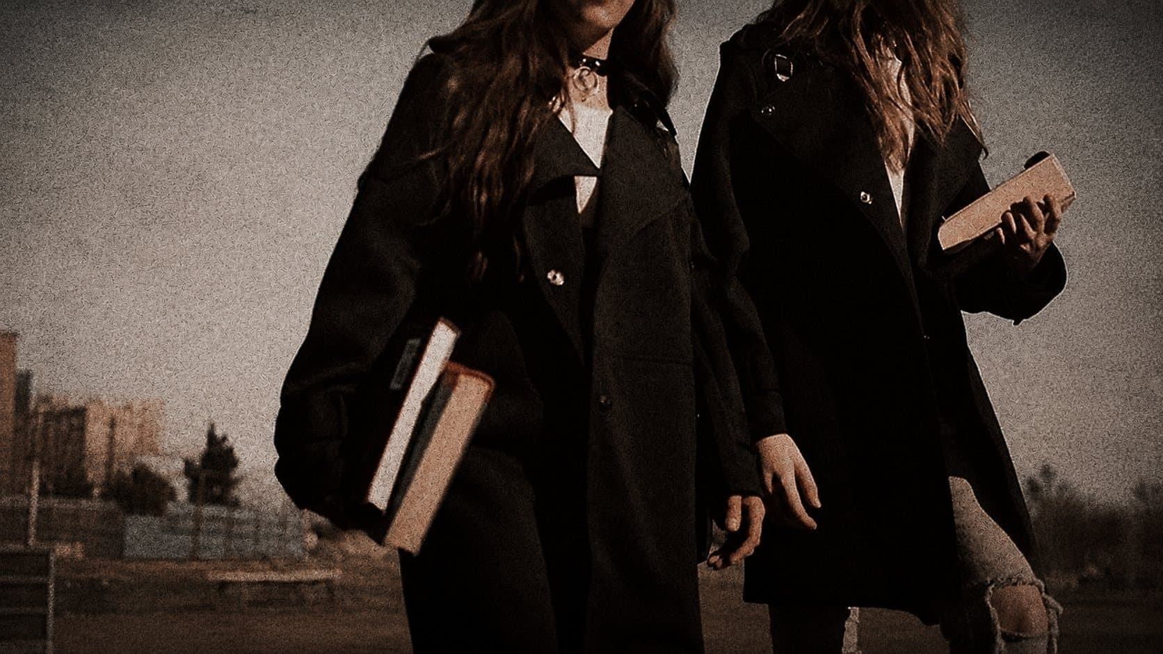 Deux étudiantes en manteau sombre, un livre sous le bras, à la tombée du jour.