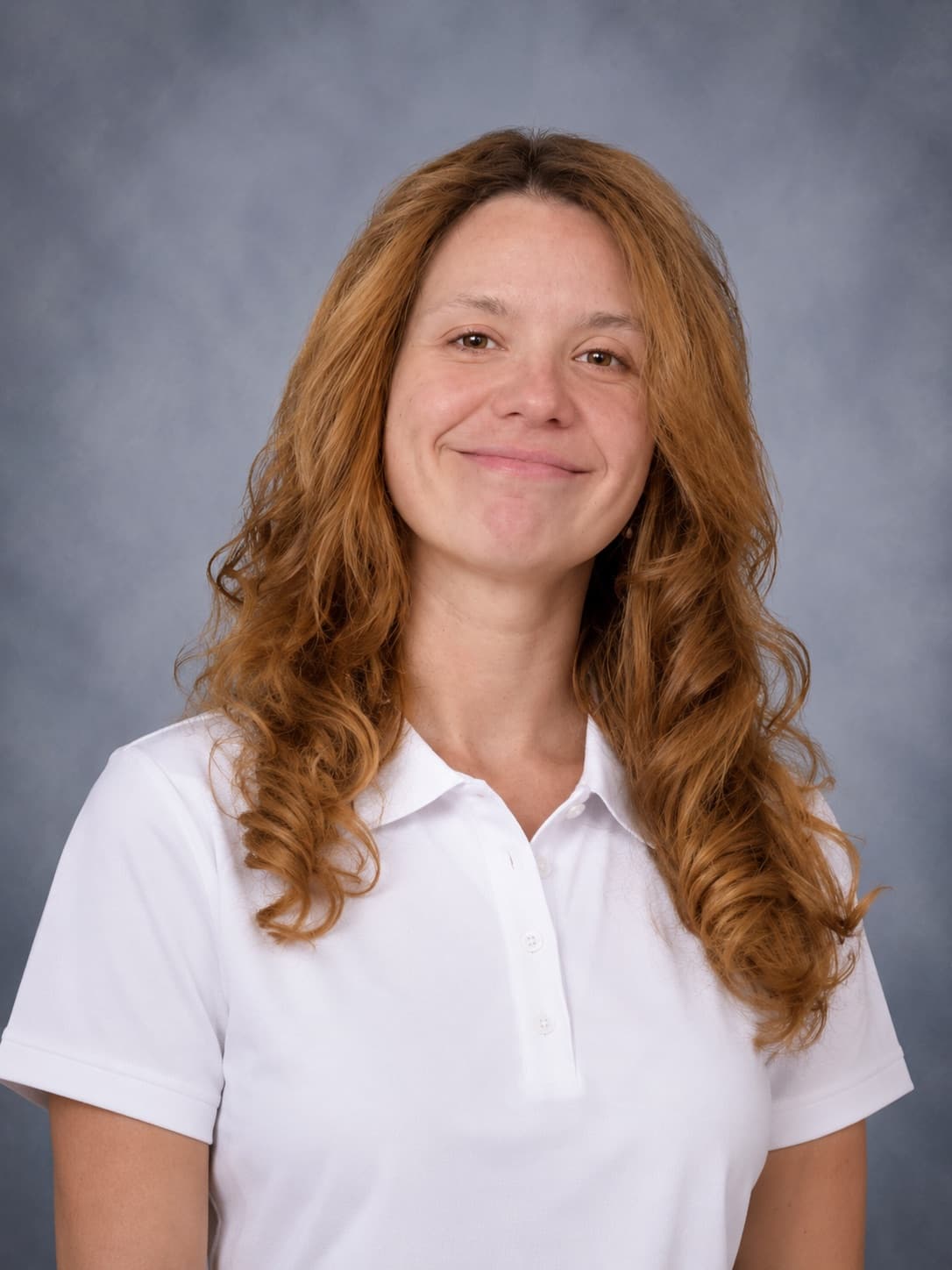 Catherine Cormier, cheveux roux bouclés, souriante, en polo blanc, devant un fond gris.